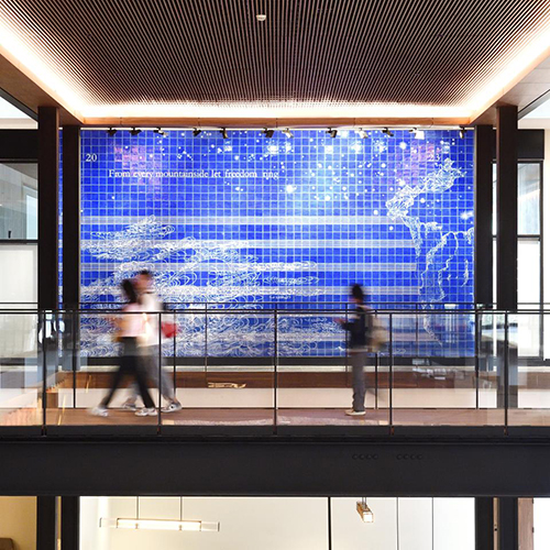 students walking in front of a large wall with blue tile art work