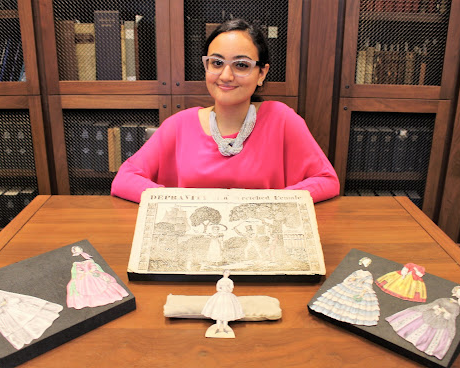 women wearing glasses seated at table with objects on display